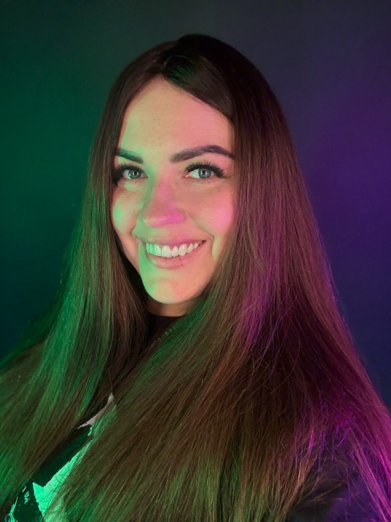 Uśmiechnięty portret młodej kobiety oświetlonej zielonym i fioletowym światłem.